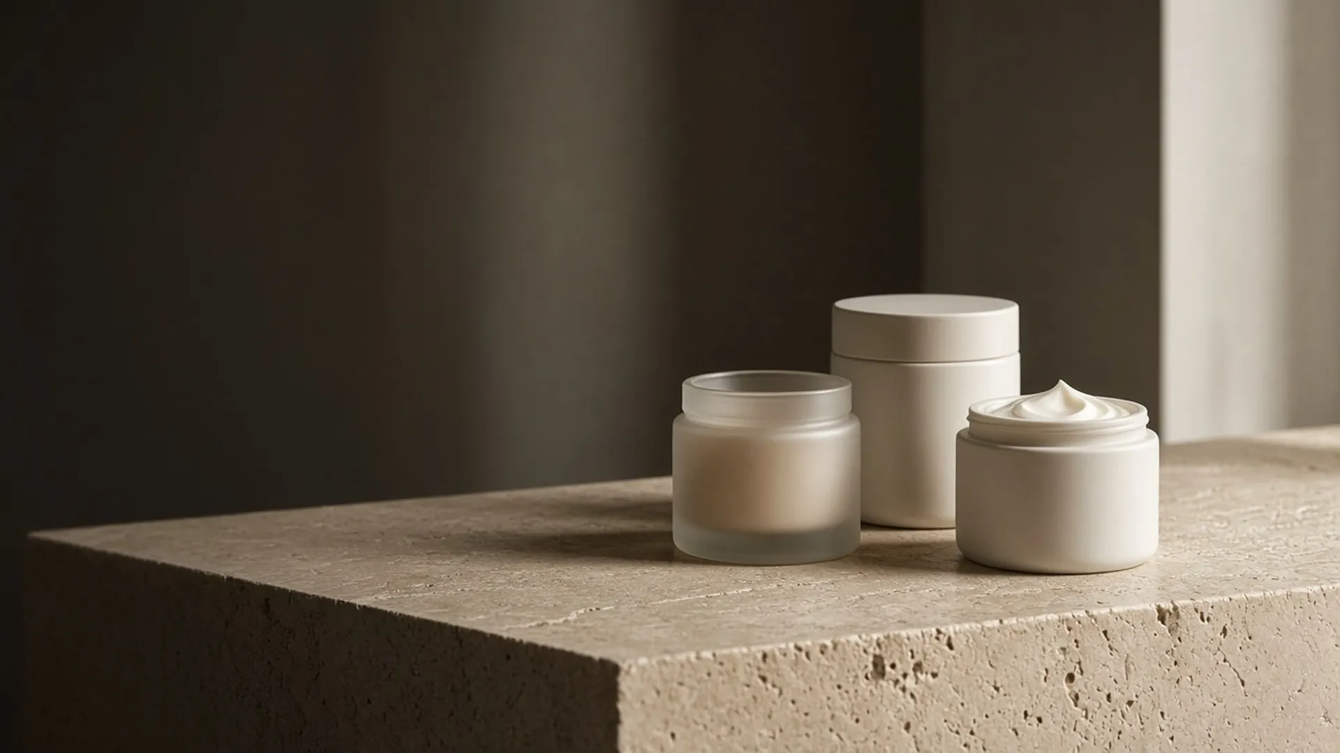 Three unlabeled cream jars on a travertine ledge