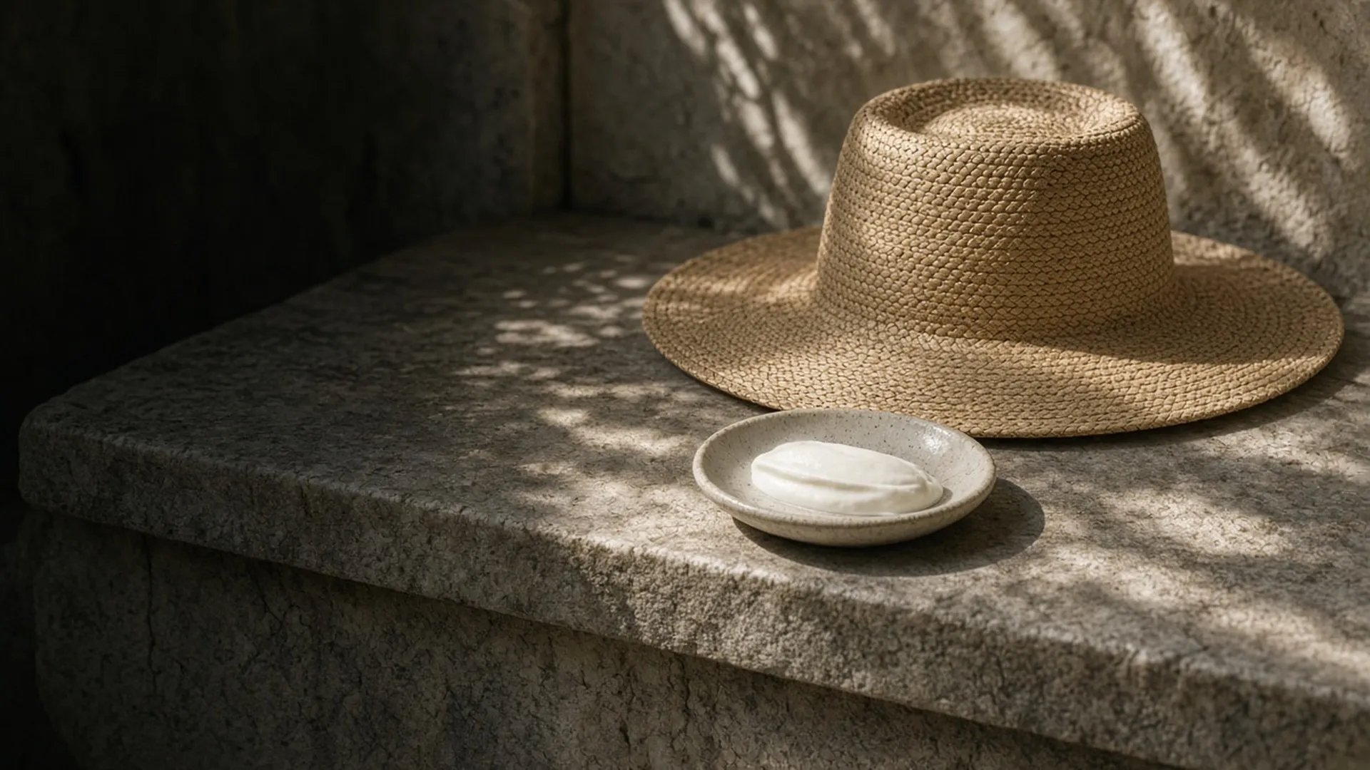 A straw hat and a dish of white cream on a shaded bench