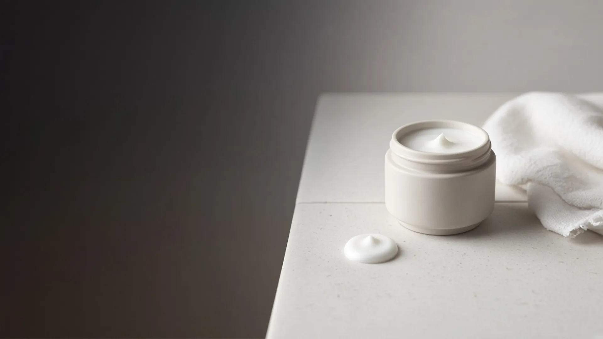 A small dab of cream on a tile beside an open jar